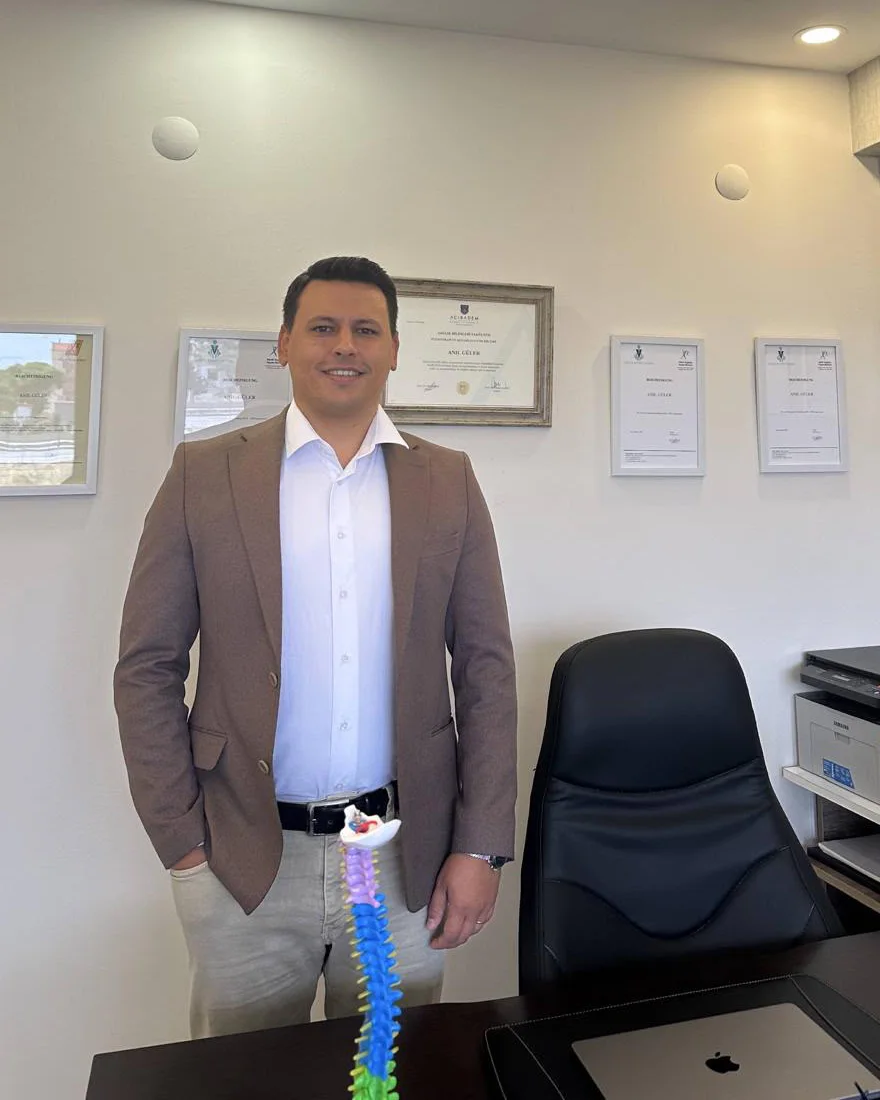 Fizyoterapist Anıl Güler, Bandırma'daki kliniğinin çalışma odasında; arkasındaki duvarda Acıbadem Üniversitesi diploması ve osteopati sertifikaları asılı
